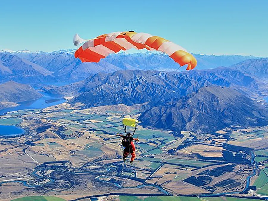 Un parachute orange et blanc au-dessus de lacs, de terres agricoles et de montagnes